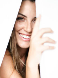 Une femme souriante qui se cache derrière un panneau blanc, capturant un moment naturel et authentiq.